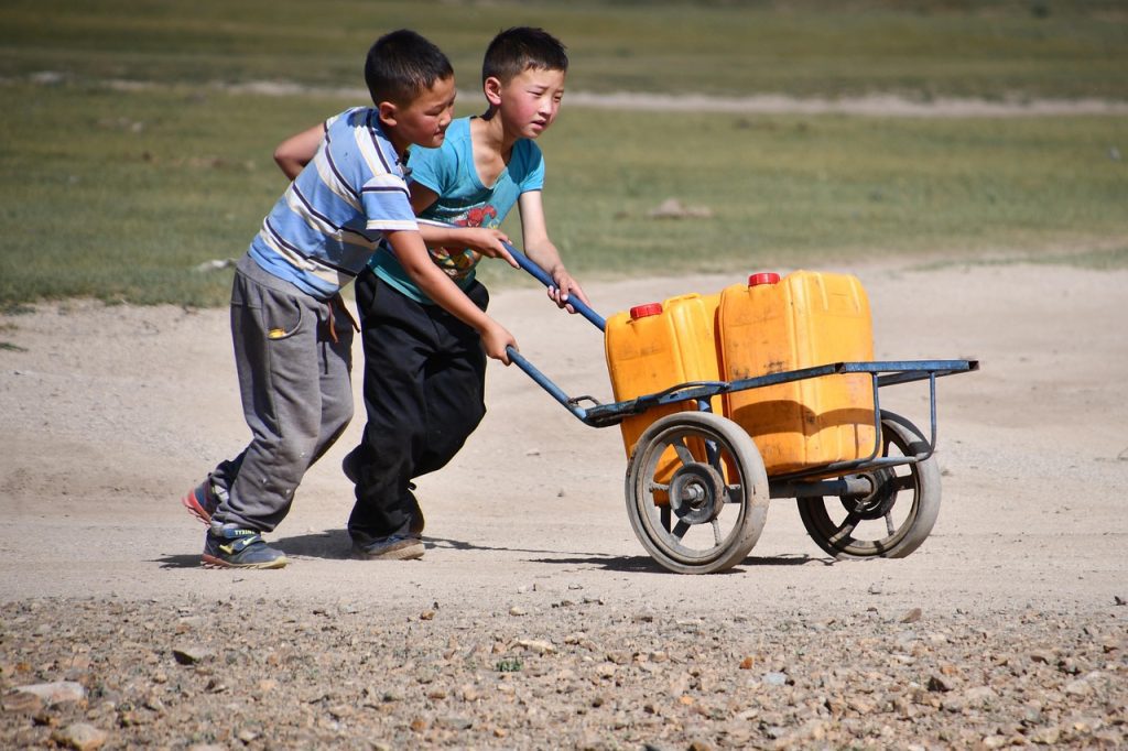 Two boys pushing a trolley of water cans